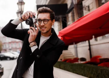 Stylish man with glasses taking photos on a film camera outdoors