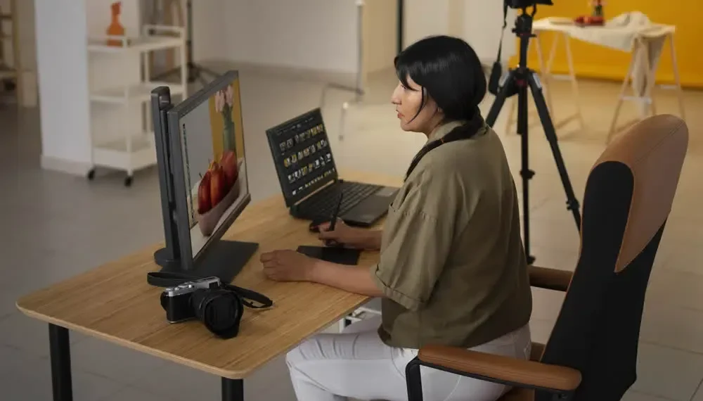 Photographer editing images at a desk with a monitor, laptop, and camera nearby