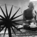 20 Iconic Photos That Shaped History: Moments That Defined Our World 61 Man seated cross-legged beside a spinning wheel, black and white