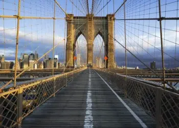 Symmetrical view of Brooklyn Bridge walkway with NYC skyline in background