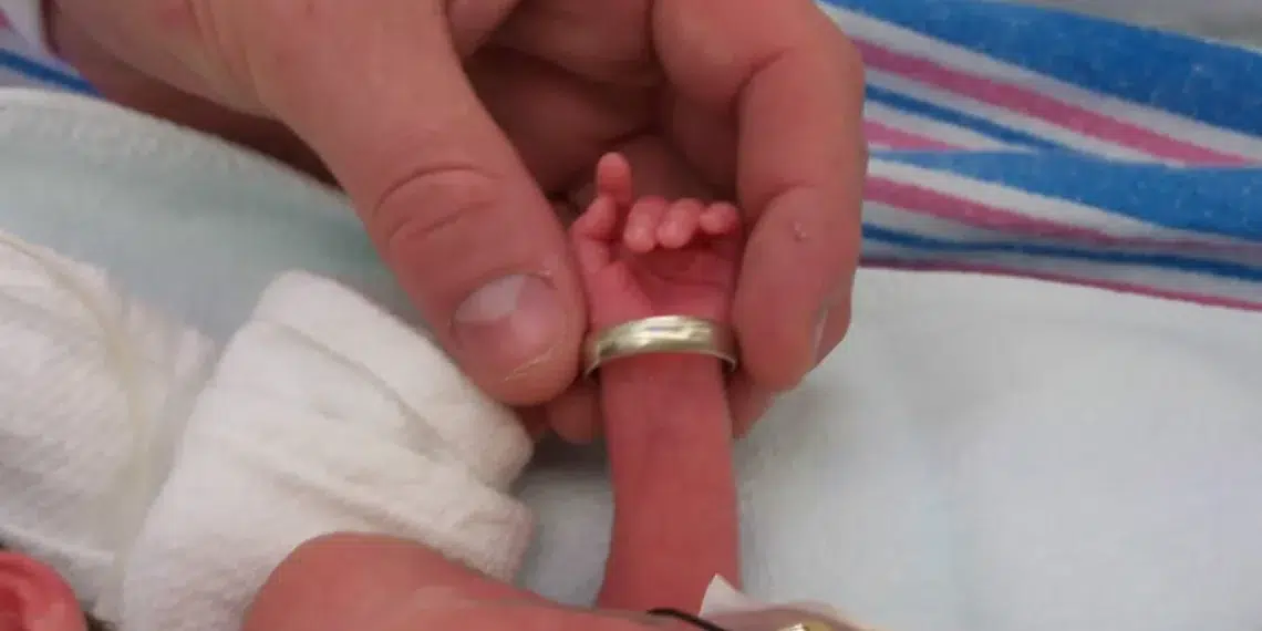 Newborn's tiny hand gripping father's wedding ring finger - storytelling photography