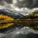 Snow-capped mountains and golden autumn trees reflected in a still lake under stormy skies
