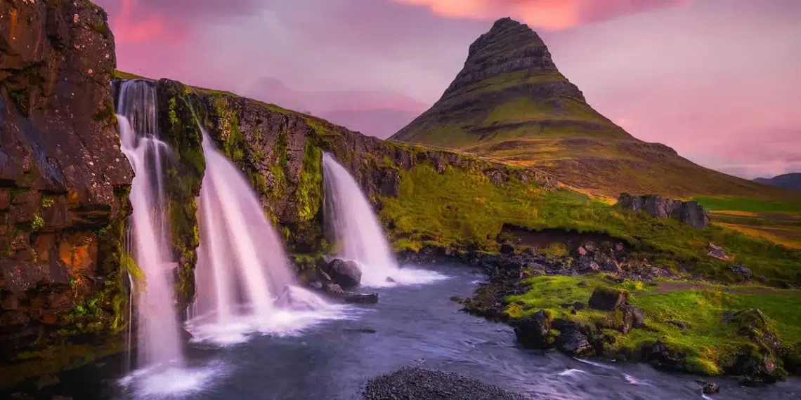 Waterfalls cascading before a iconic peaked mountain under a vivid pink sunset sky
