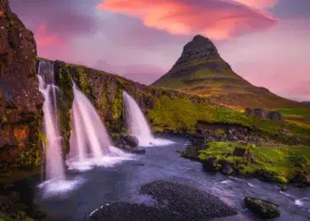 Waterfalls cascading before a iconic peaked mountain under a vivid pink sunset sky