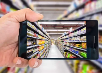 Hand holding a smartphone photographing a supermarket aisle with shelves