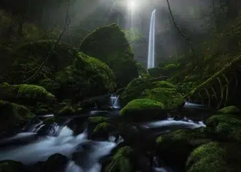 Tall waterfall with mossy rocks and misty forest stream, landscape photos around the world