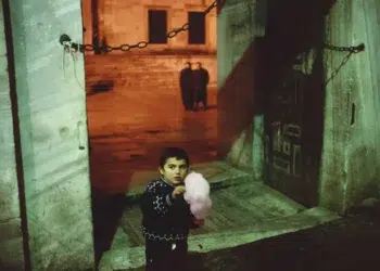 Child holding cotton candy at night near stone gateway, legendary color photography