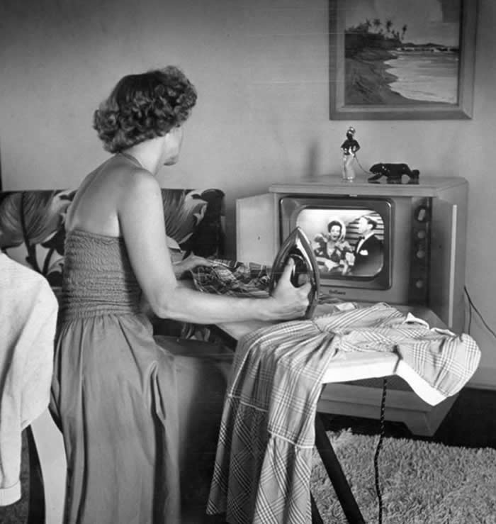 A multitasking mother ironing clothes while watching television, a common way to pass the time during household chores, 1950s