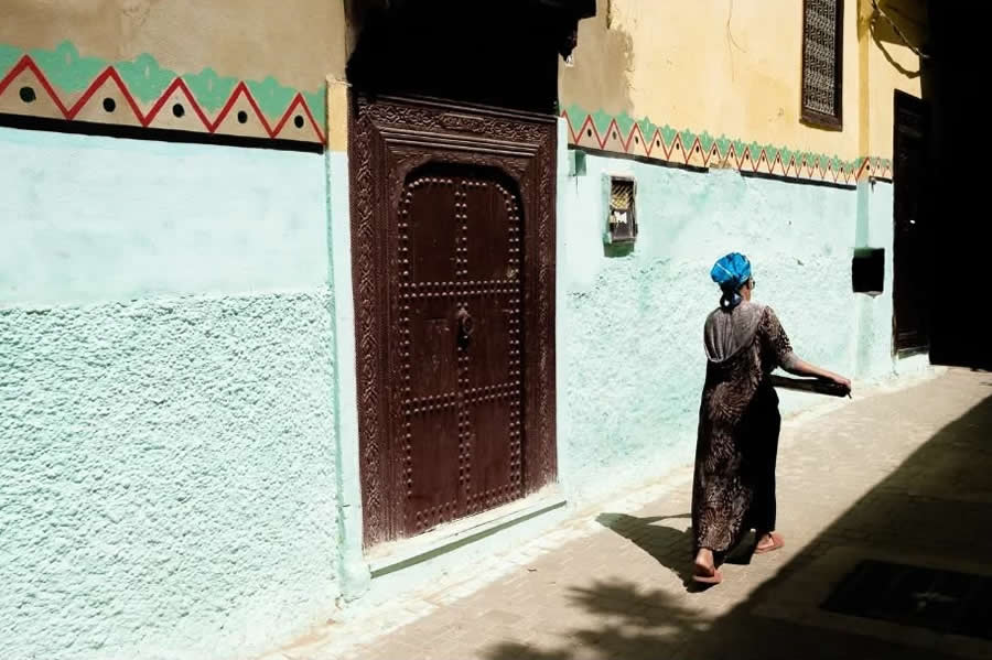 Lady Walking in Morocco Street with Tradition House and Shadows - Captivating Street Photography by Giancarlo Zuccarone