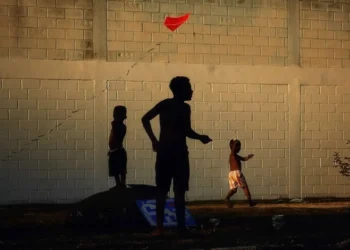 Children's silhouettes flying a red kite against a brick wall