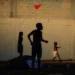 Children's silhouettes flying a red kite against a brick wall