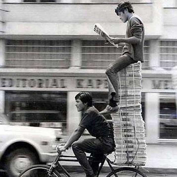 Two boys riding bicycles while delivering newspapers - Black and White Bicycle Photos of Everyday Life