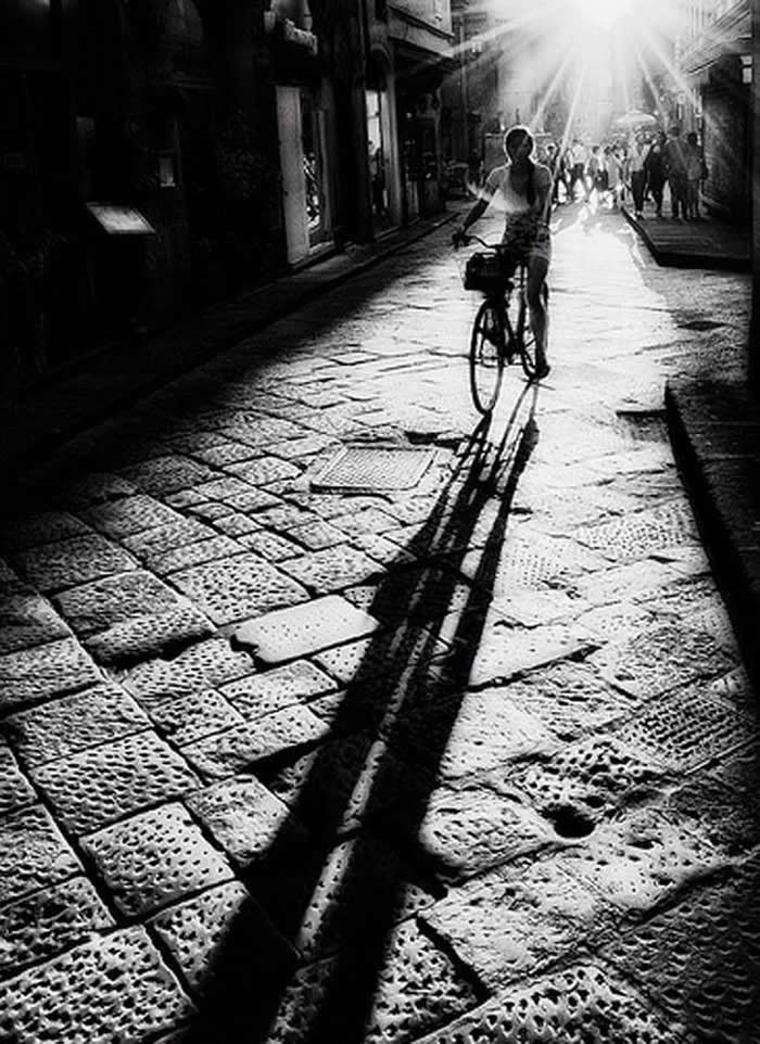 Cyclist riding through sun rays on a city street - Black and White Bicycle Photos of Everyday Life