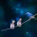 A blue bird perched on a branch beside two fluffy chicks begging for food with open beaks