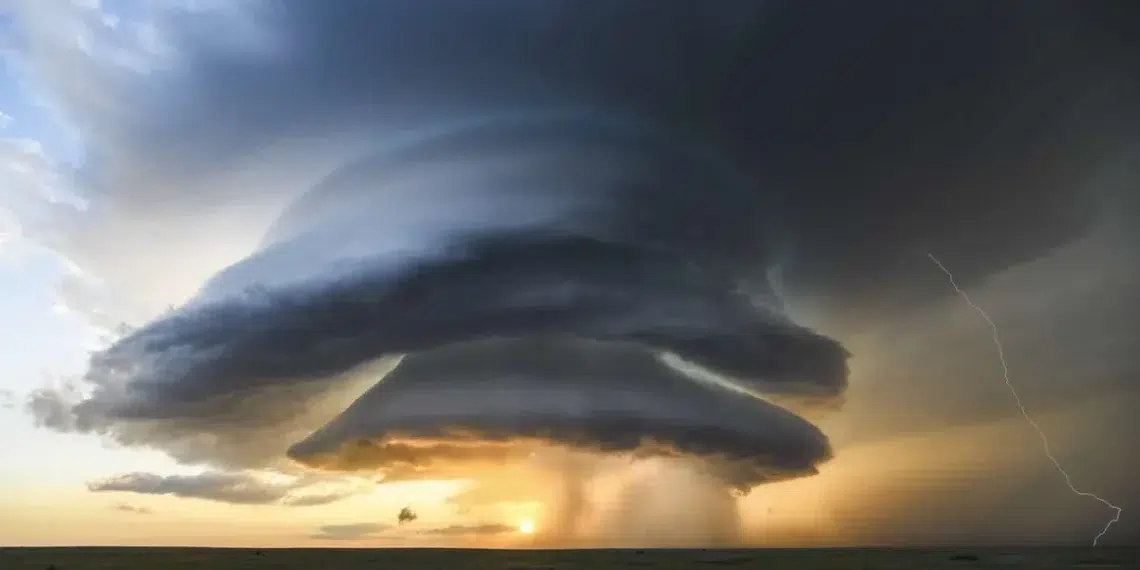 A massive supercell storm with lightning over a flat grassland at sunset