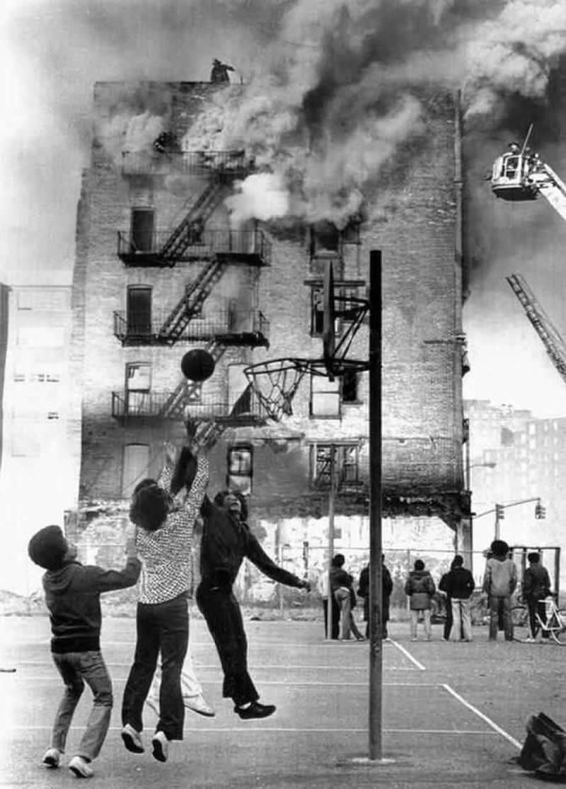 Firemen put out blaze at a building on 101st Street at First Avenue burned in 1975 while children play basketball, Harlem, New York City. Photo by Paul Hosefros. - Rare Historical Photos That Bring Forgotten Moments