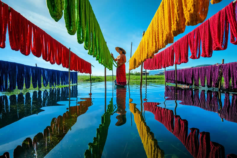 Colorful fabrics with a beautiful reflection. A woman at work by Inle Lake while colorful fabrics dry - Travel and Cuture Photography by Erdem Kilic