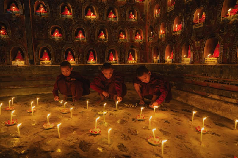 In Buddhism, a candle is not just light; it is wisdom dispelling ignorance. Surrounded by flames, the novice monk learns that enlightenment begins within. - Travel and Cuture Photography by Erdem Kilic