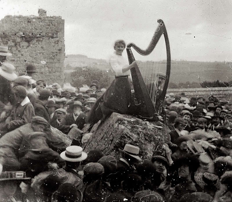 A young woman playing a harp to a large crowd, Rock of Cashel, Ireland, ca. 1910 - History Forgotten Moments Unseen Photos