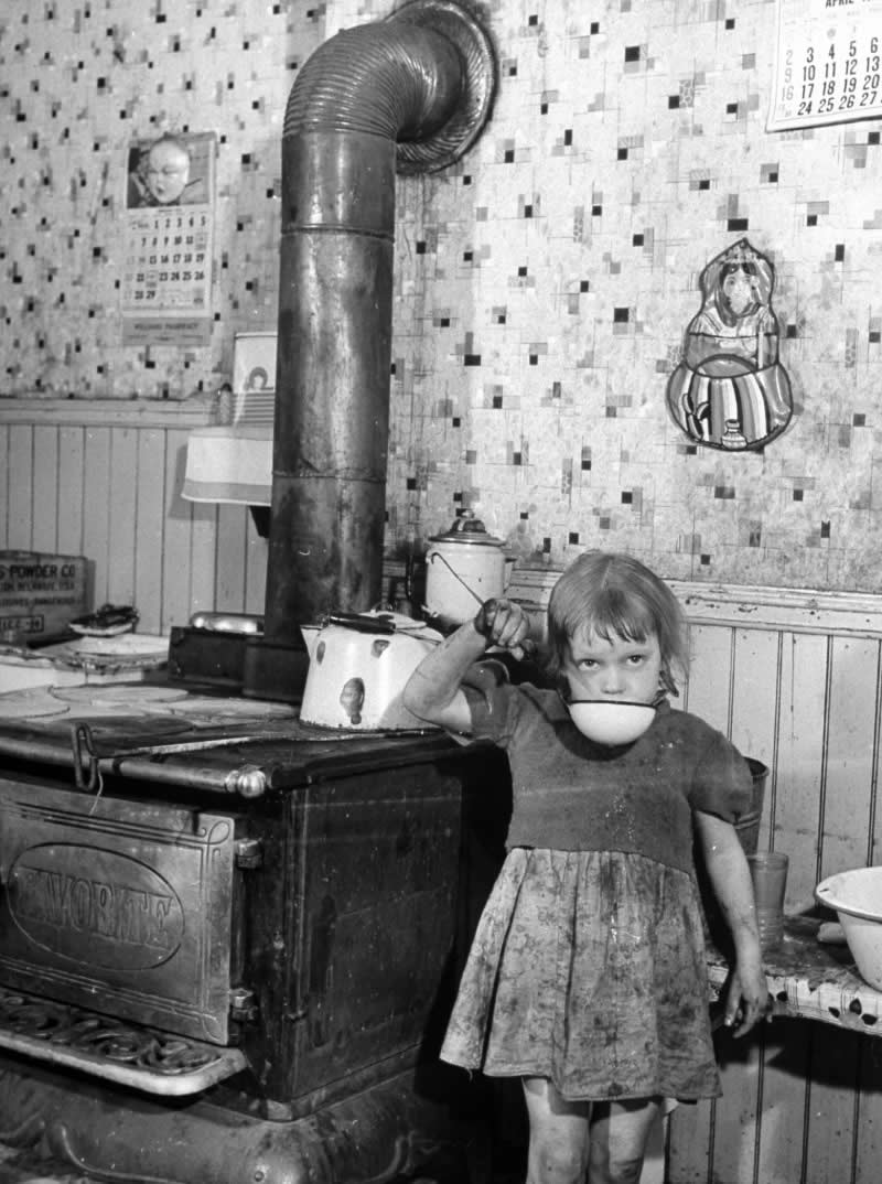 A poor steelworker's little girl, her face and clothes dirty from the day playing outside, drinks water from a dipper in their small kitchen in Pittsburgh, 1940s - History Forgotten Moments Unseen Photos