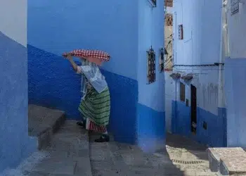 A woman carrying a bundle through a narrow blue-walled alley in Chefchaouen, Morocco