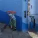 A woman carrying a bundle through a narrow blue-walled alley in Chefchaouen, Morocco