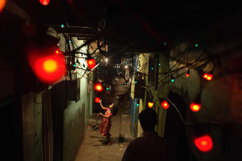 A child in Dharavi, India, plays with red lights that decorate a street for an upcoming wedding by Jonas Bendiksen - Most Iconic Photos From the National Geographic Archives