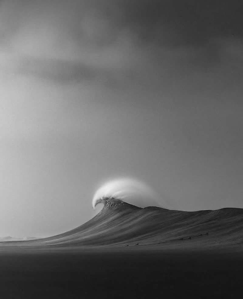 Timeless and Emotional: 30 Black and White Photos That Touch the Soul 45 Black and white minimalist photo of a large ocean wave rising and curling in the distance, captured with smooth tones and a vast open sky that emphasizes the calm yet powerful motion of the sea.