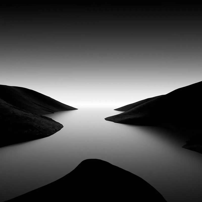 Timeless and Emotional: 30 Black and White Photos That Touch the Soul 49 Black and white minimalist landscape of dark hills surrounding a smooth, misty body of water that fades into the horizon, creating a serene scene of symmetry, silence, and endless depth.