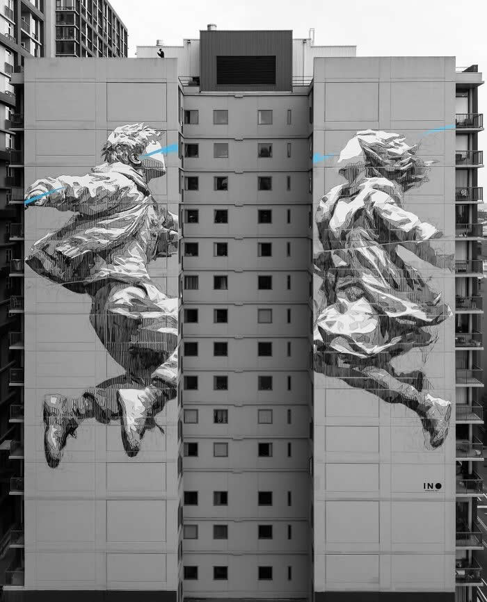 A striking black-and-white mural of two figures leaping across the facades of adjacent buildings, creating the illusion of motion and connection over the urban gap between structures. Seattle, USA.