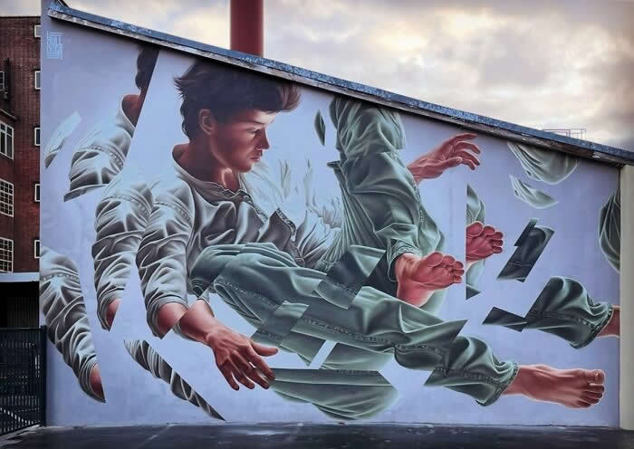 A surreal mural of a young man appearing to fall or float through broken geometric layers, with multiple fragmented versions of his body creating a dynamic illusion on a curved building wall. Berlin, Germany.