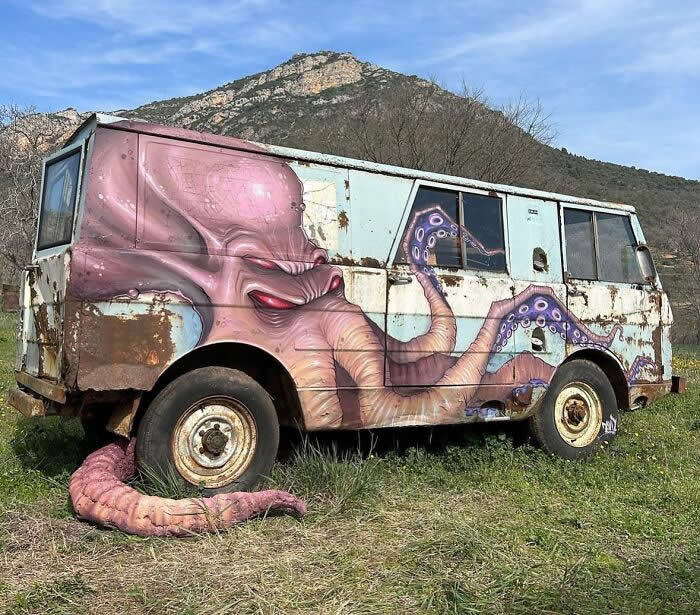 A rusted old bus transformed into street art with a giant octopus painted across its body, its tentacles wrapping around the vehicle and extending onto the ground in a surreal outdoor setting. Spain.