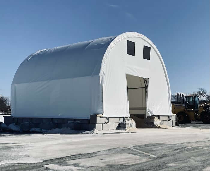 30 Public Objects Having a Total Meltdown 41 A large white storage building with two square vents resembling eyes and a wide open doorway forming a smiling mouth, creating a cheerful face-like appearance in a snowy outdoor industrial yard.