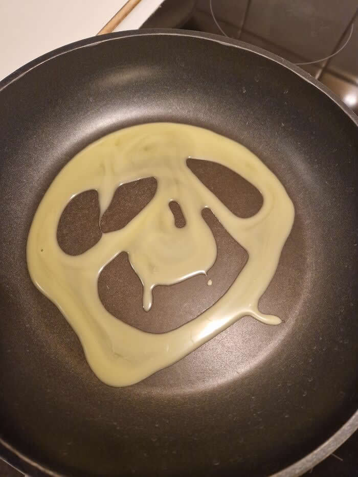 30 Public Objects Having a Total Meltdown 46 Melted butter spreading in a frying pan forming a smiling face-like shape with two eye holes and a curved mouth, creating a funny pareidolia expression while heating on the stovetop.