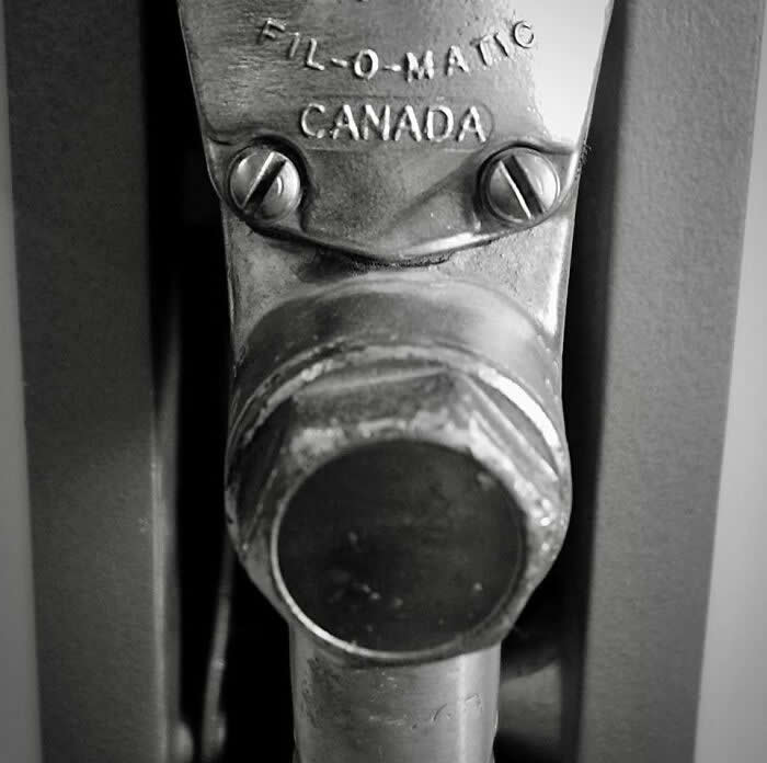 30 Public Objects Having a Total Meltdown 51 A metal mechanical part labeled “FIL-O-MATIC CANADA” with two screws resembling eyes and a round protruding piece like a dog’s nose, creating a funny face that looks like a cartoon dog.