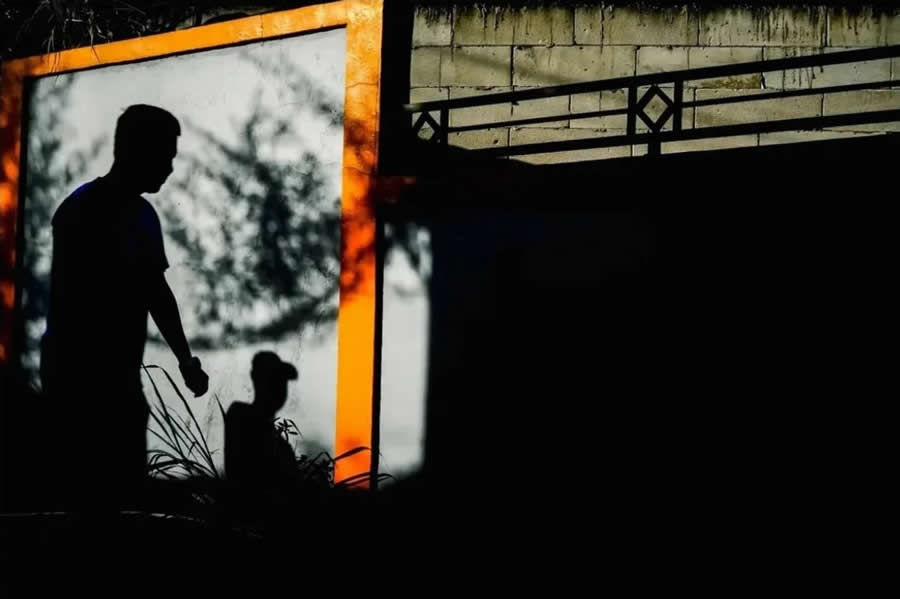 Silhouettes of two people framed within a bright orange border against a shadowy background, creating strong contrast and layered composition in a dramatic street photography scene.