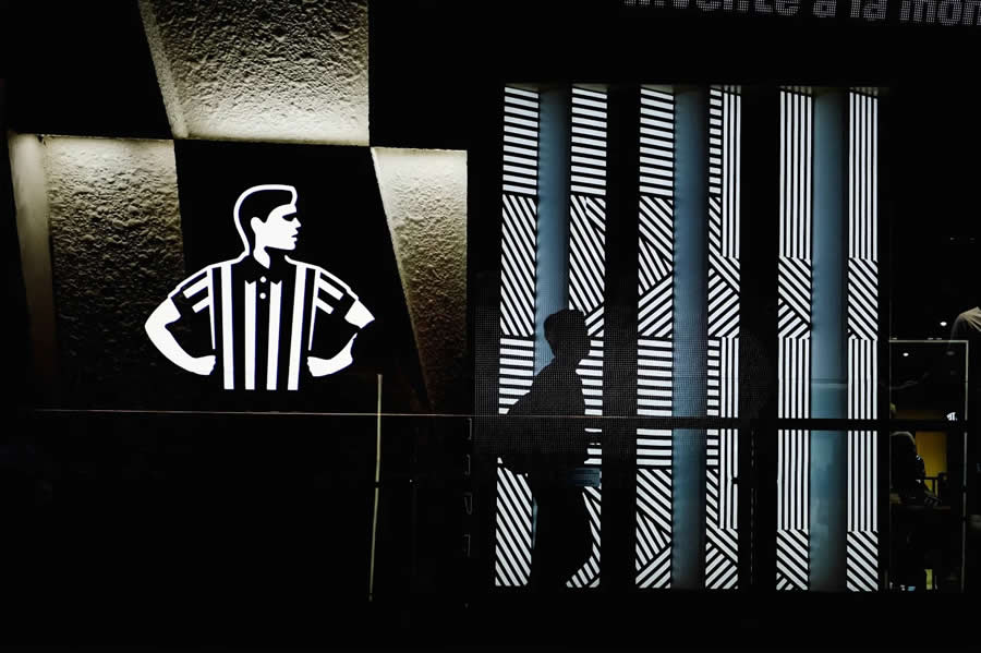Silhouette of a person walking past a wall with bold black and white striped patterns and a graphic sign, creating a high-contrast, geometric street photography composition.
