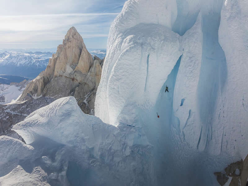 A solo climber scaling a steep icy wall on Cerro Torre surrounded by massive glaciers and rugged mountain peaks.