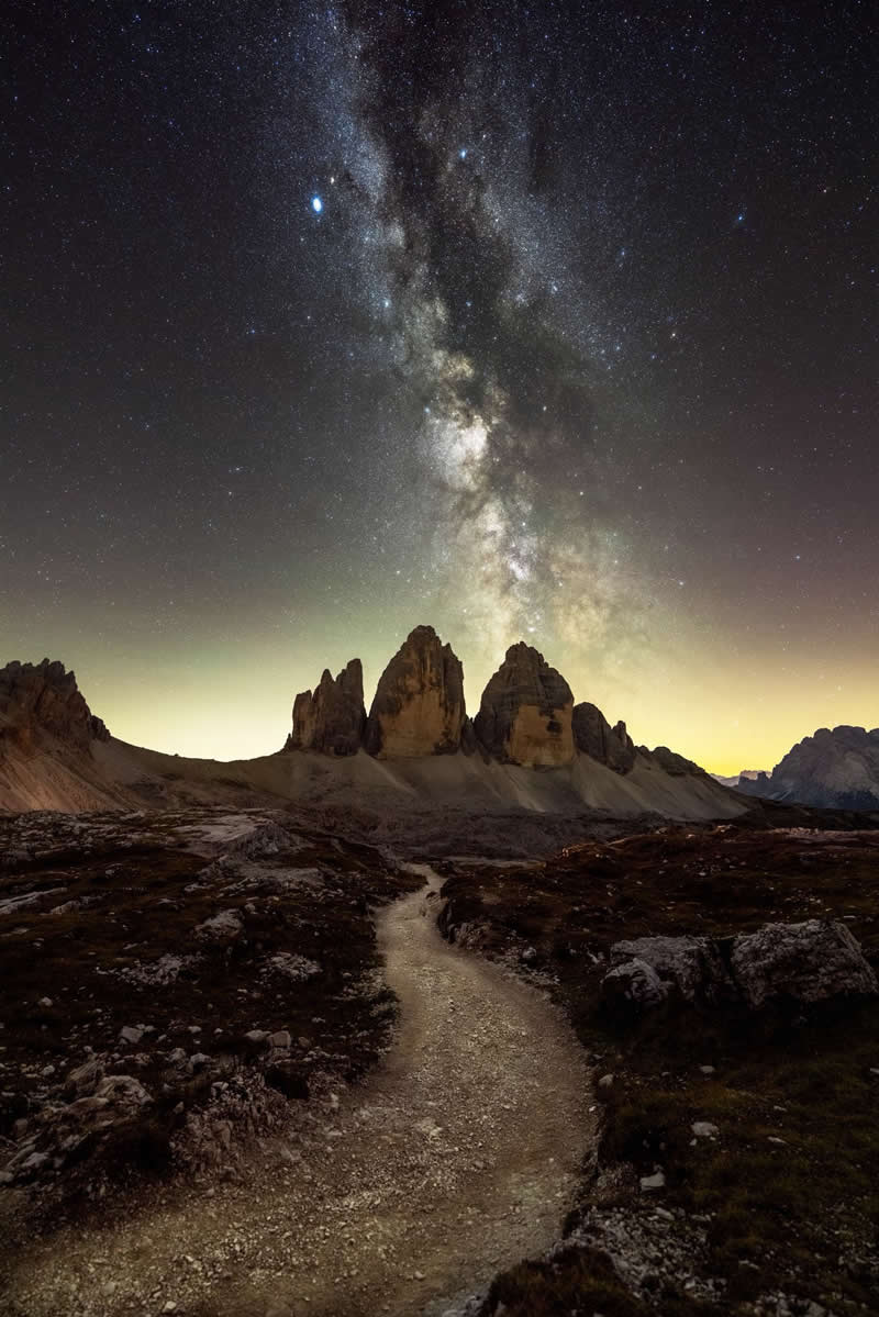 Beyond the Stars: How Mads Peter Iversen Captures the Milky Way Like No One Else 28 The Milky Way stretches above jagged mountain peaks, while a winding trail cuts through the landscape below, all beneath a sky bursting with stars.