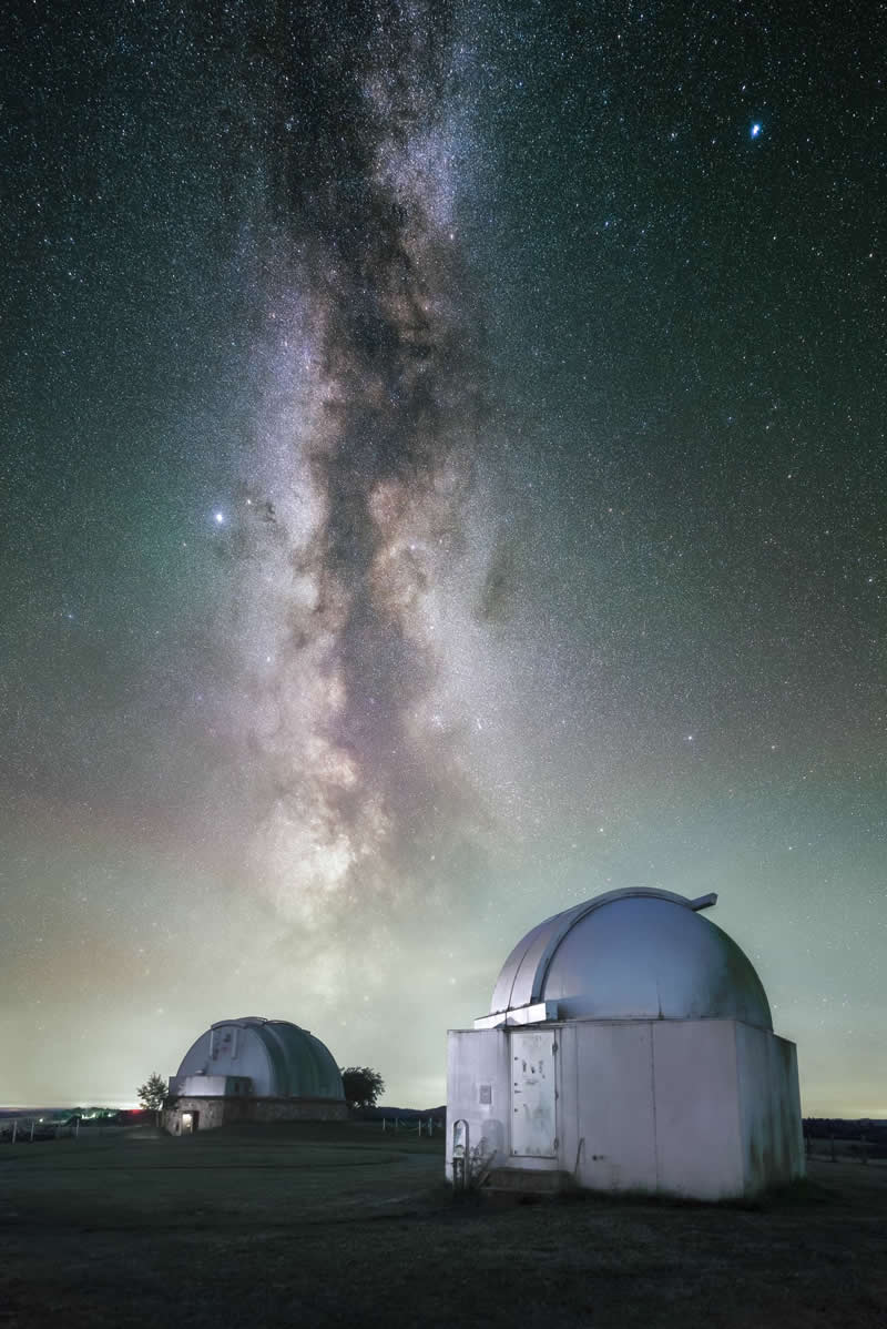 Beyond the Stars: How Mads Peter Iversen Captures the Milky Way Like No One Else 38 Astronomical observatories beneath the Milky Way galaxy with thousands of stars visible in the night sky above the domed telescope buildings.
