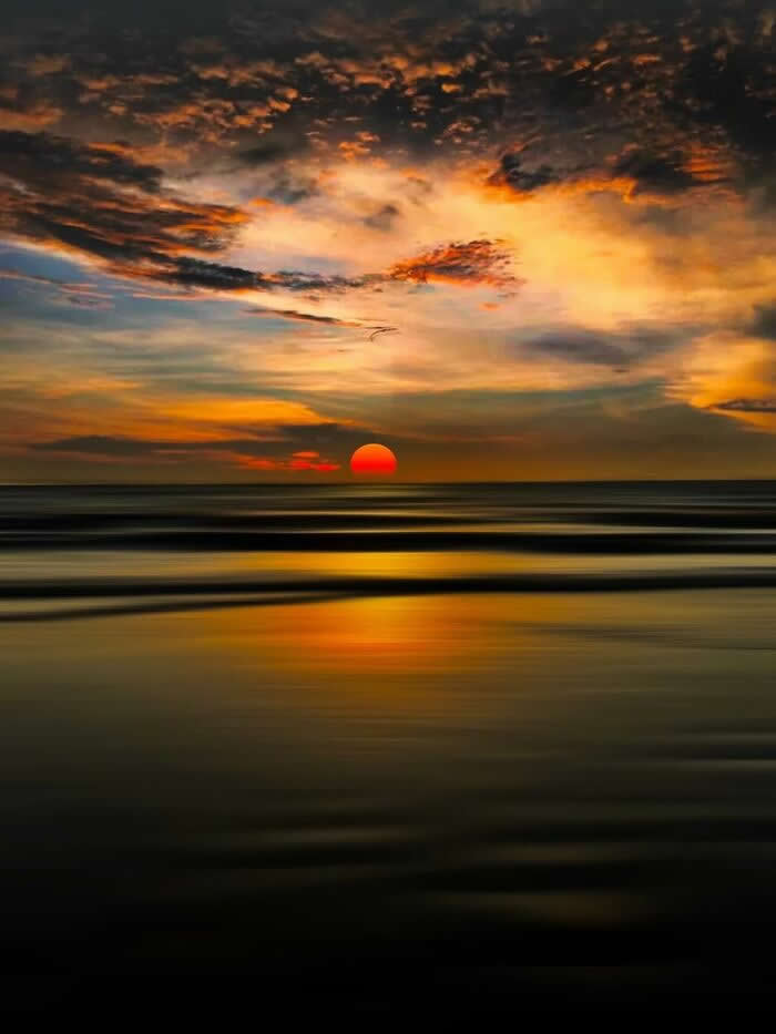 Crimson sunset over the ocean with dramatic golden clouds and smooth reflective water creating a peaceful seascape at twilight.