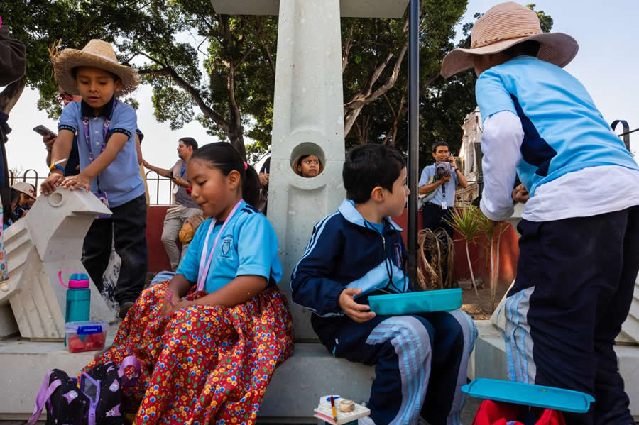 Children sitting and playing around a concrete structure in a park, with one child&rsquo;s face peeking through a circular hole, creating a layered and colorful street photography scene full of interaction and expression. - Mexico Street Photography by Tavepong Pratoomwong