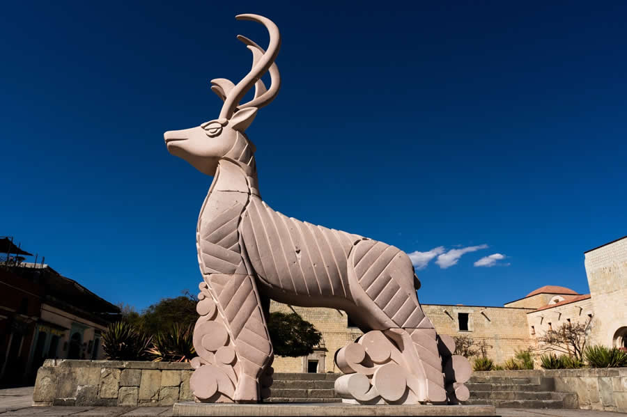 Deer sculpture in an open plaza with clouds positioned behind its antlers, creating a visual juxtaposition against a deep blue sky, captured in a minimal and well-composed street photography scene. - Mexico Street Photography by Tavepong Pratoomwong