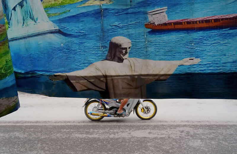 Street photo of a cyclist passing behind a mural, creating an illusion where the painted figure appears to be riding the bicycle.