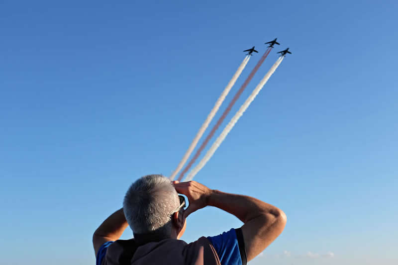 Street photo of a man looking at planes in the sky, aligned so the aircraft trails appear to come from his hands, creating a visual illusion.