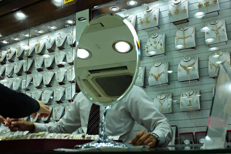 Street photo inside a jewelry shop where a mirror aligns with a man’s head, creating an illusion of a face using reflections of ceiling lights.