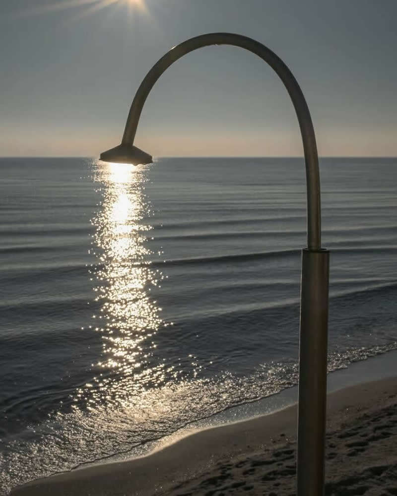 Street photo of a beach shower aligned with sunlight reflecting on the ocean, creating an illusion that water is flowing from the showerhead.