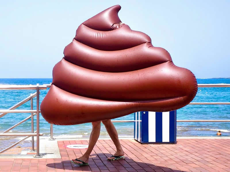 A person walking along a seaside promenade is hidden inside a large brown inflatable, with only legs visible, creating a humorous illusion.