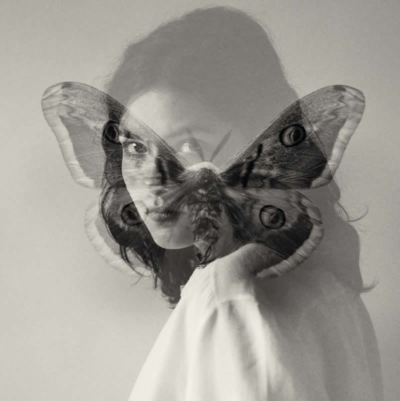 Black and white double exposure portrait of a woman with a butterfly overlay across her face, blending human emotion with nature in a surreal, fine art composition.