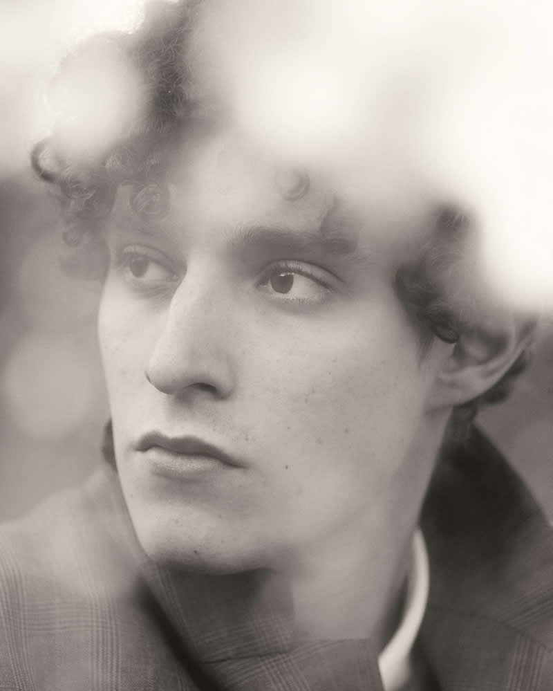 Soft-focus black and white close-up portrait of a person with curly hair, partially obscured by a hazy overlay, creating a dreamy and introspective mood.